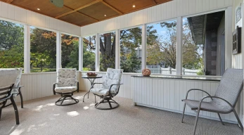 Interior de porche acristalado con vistas al jardín y zona de asientos